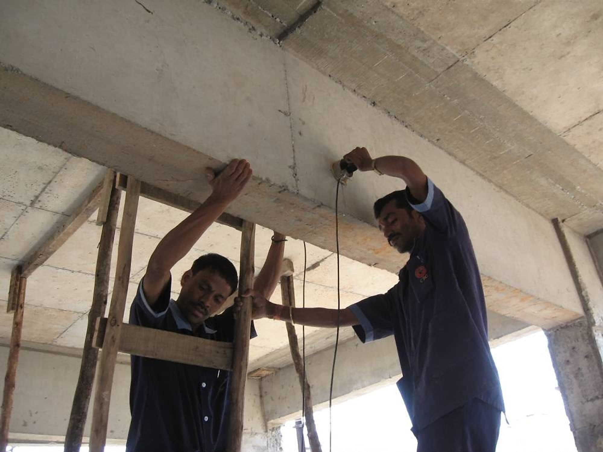 Two technicians holding an ultrasonic pulse velocity test against the underside of a concrete beam