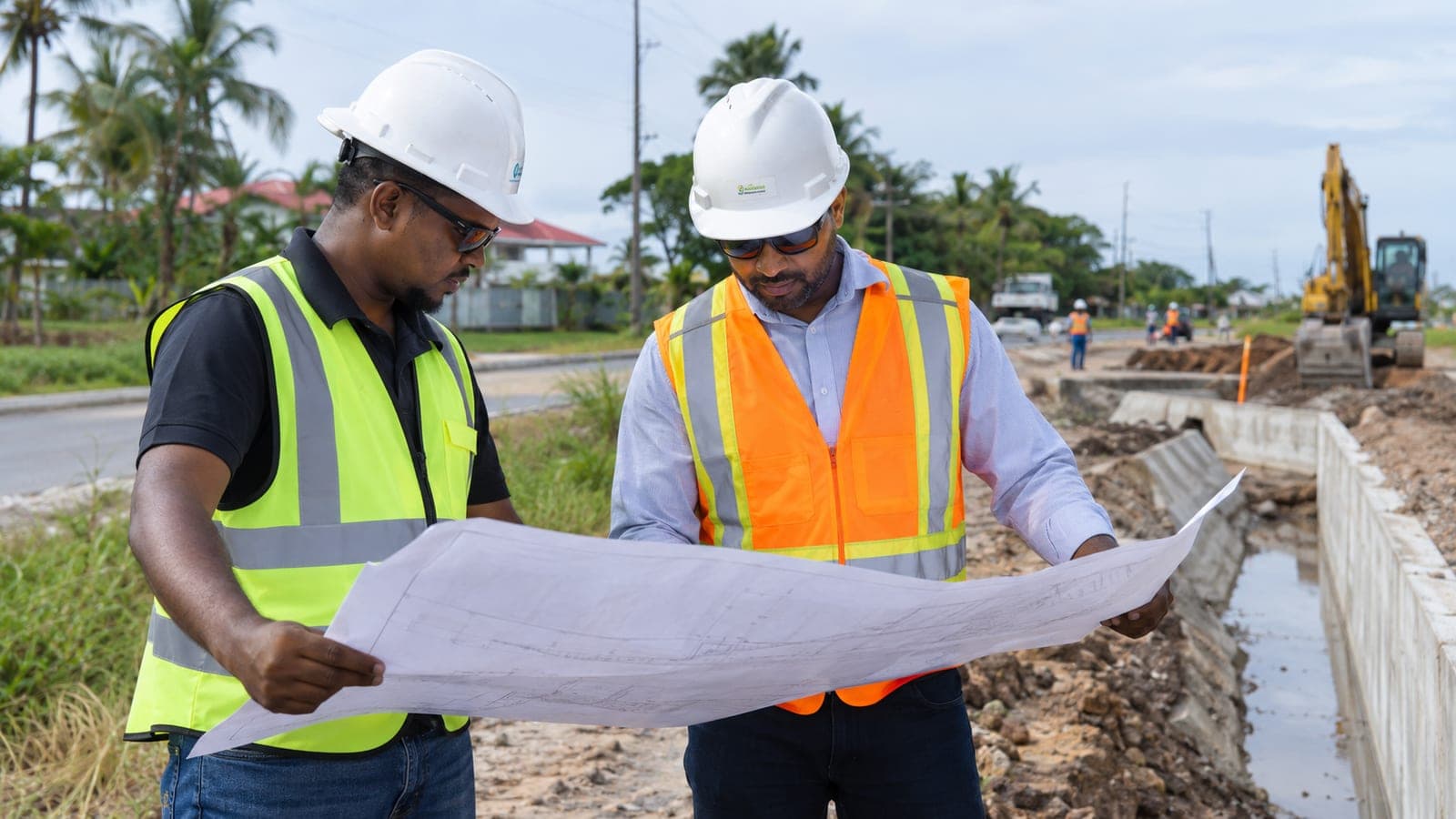 Two engineers reviewing plans beside a drainage channel and road works